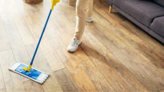 A handsome man in cozy homewear cleans a wooden floor with a mop.