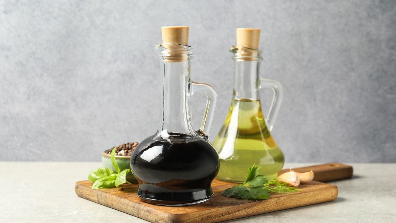 Balsamic vinegar in glass jug, oil, herbs and spices on gray textured table