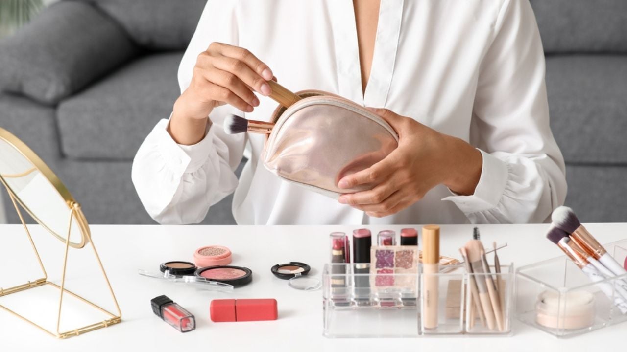 Beautiful young African-American woman with cosmetic bag doing makeup at home, closeup