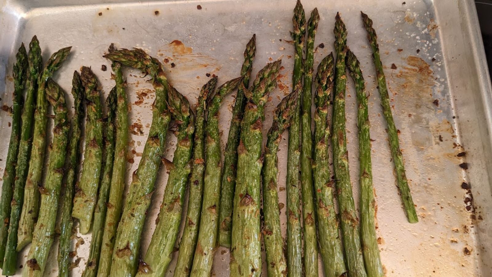 An aluminum sheet pan with broiled asparagus.