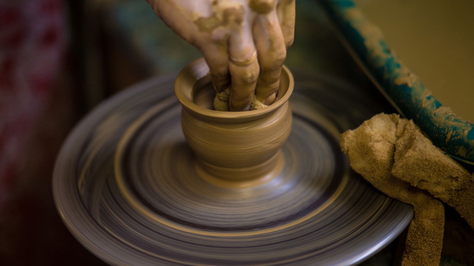Close-up hands of potter in apron making vase from clay