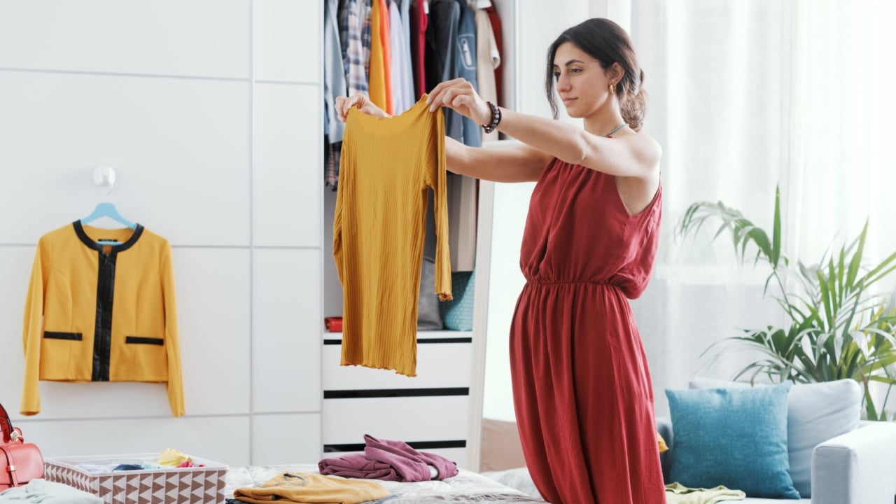Elegant woman in her bedroom, she is decluttering her wardrobe and choosing clothes