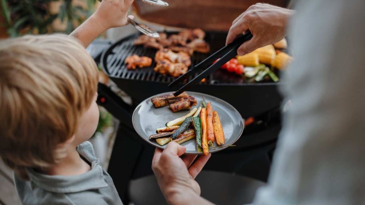 grilling ribs and vegetable on grill during family summer garden party, close-up
