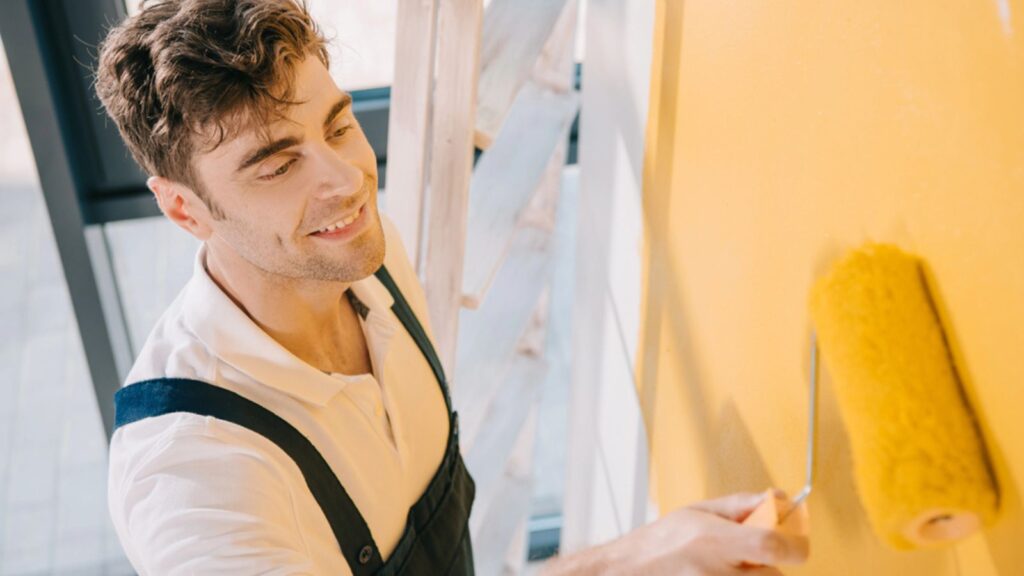 man smiling while painting wall in yellow color