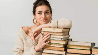 a young woman smiles with a stack of books