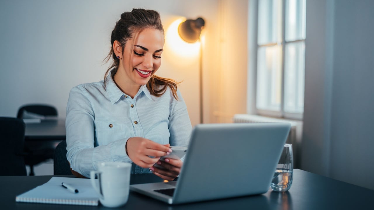 Typing business message. Confident young woman holding smart phone and looking at it with smile.