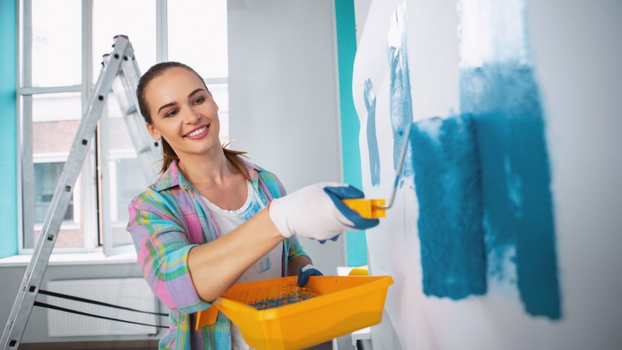 My leisure. Exuberant dark-haired woman holding a roller and painting the walls