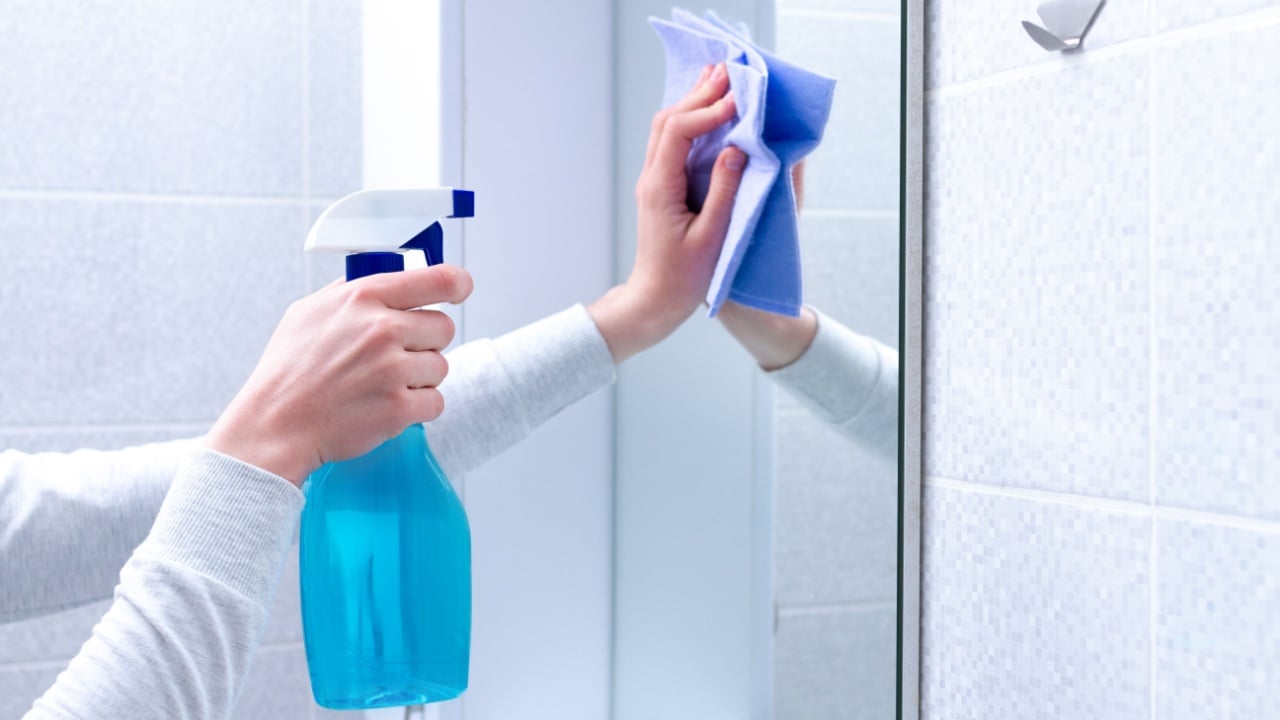 Cleaning and polish mirror with rag and spray in bathroom at home. Housekeeping and cleaning service. Clean house, cleanliness
