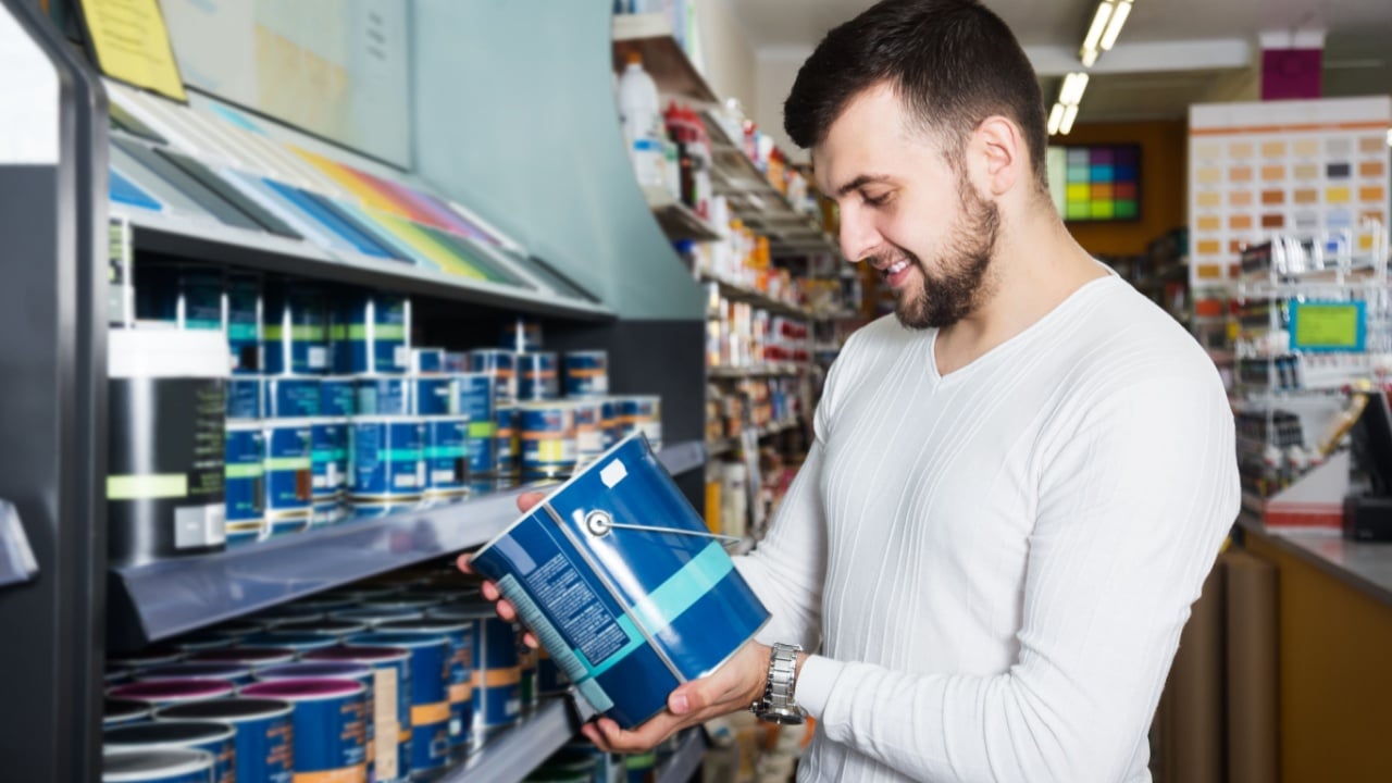 Smiling man choosing new wall paint in paint supplies store