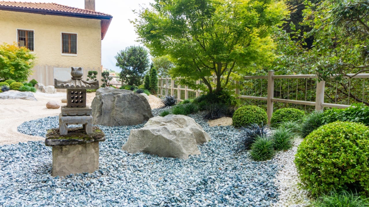 Charming Japanese-style garden with traditional attributes: Oki-gata lantern, gravel paths, boxwood trimmed bushes, maple trees. Landscaping photo of japanese garden.
