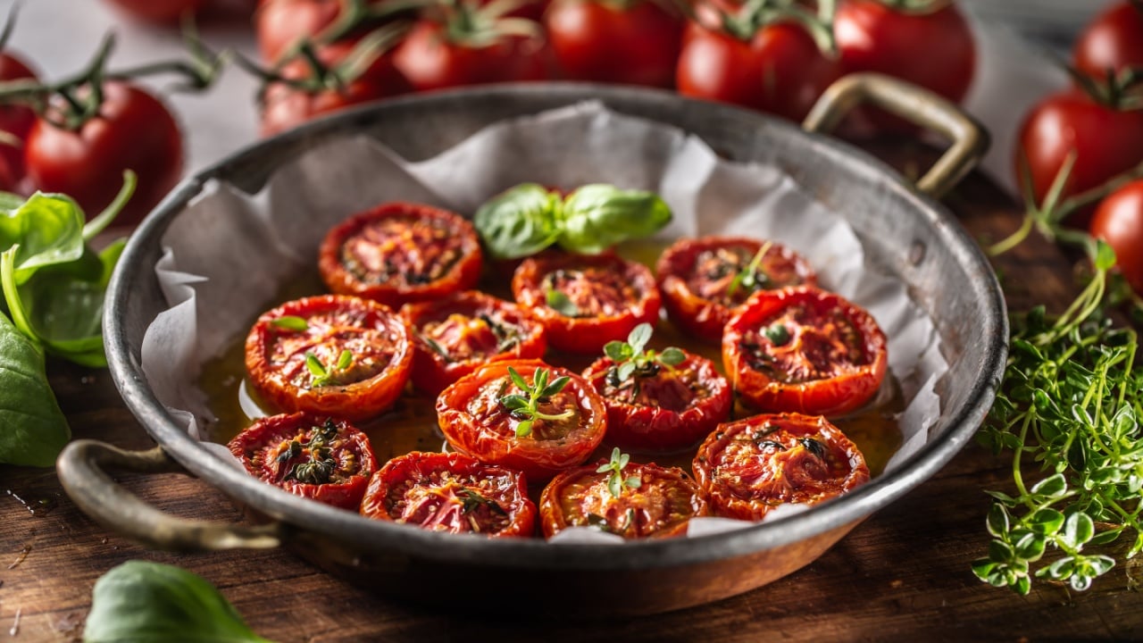 Roasted tomatoes with olive oil thyme oregano and basil in pan.