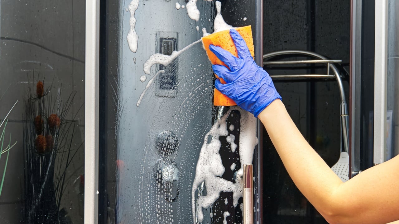 Cleaning of shower steam cabins from calcium deposits. Cleaning in the bathroom. hand in gloves with rag and detergent washing shower and glass