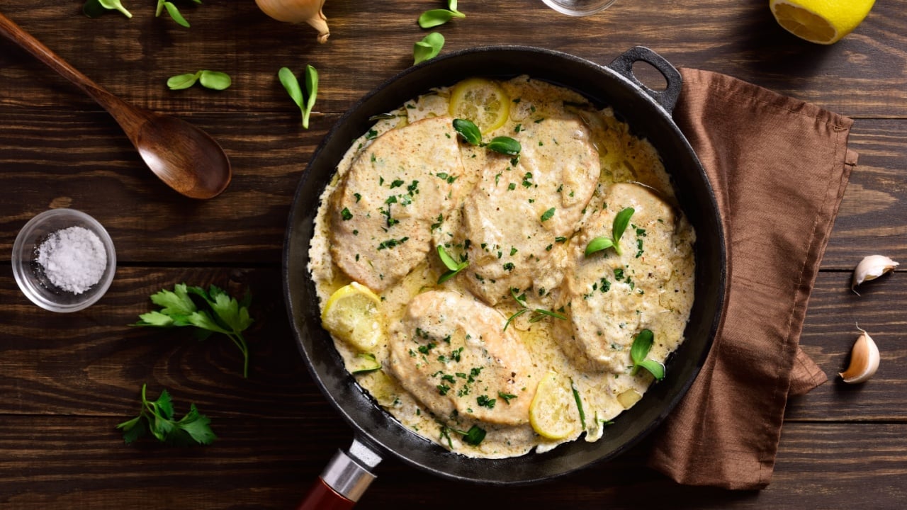 Chicken breast in creamy garlic sauce in cast iron pan over wooden background. Healthy diet food. Top view, flat lay