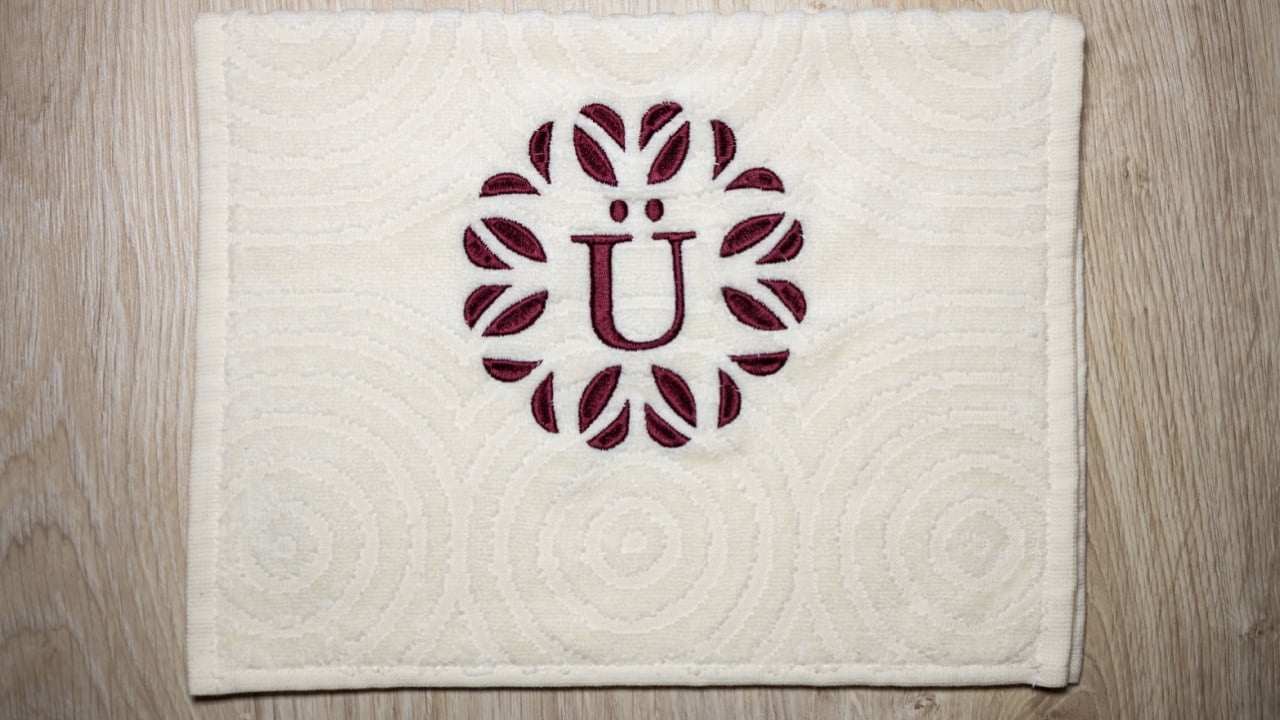 Embroidery design, alphabet monogram E and &Uuml;. Machine Embroidery on a cotton towel with burgundy color.