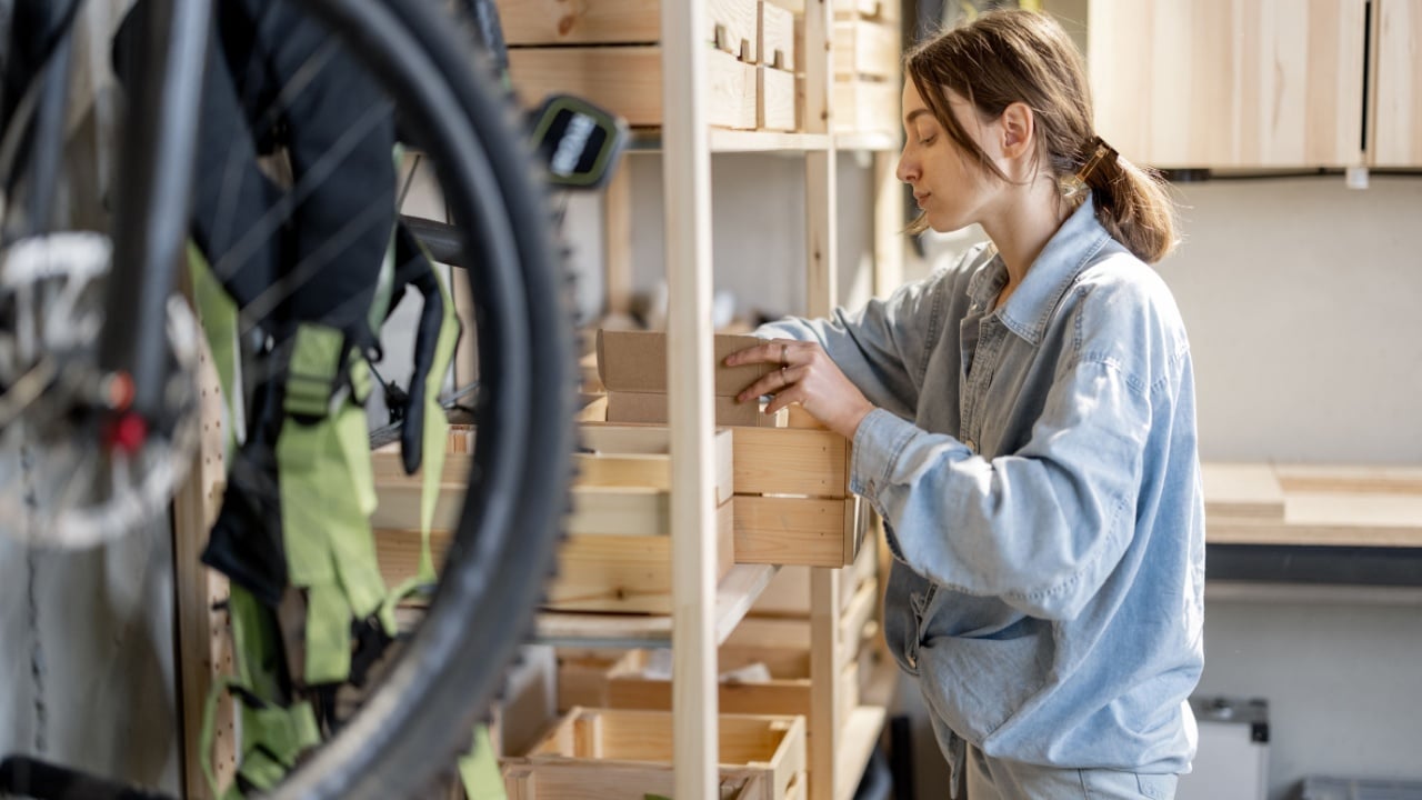 Young handywoman searching some working tools on a wooden shelves in the workshop. Concept of organization in home workshop or storage