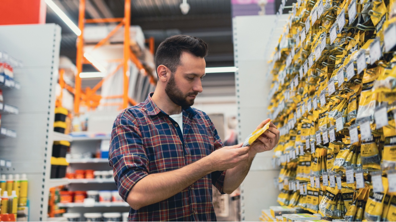 a man chooses a product in a building materials store next to a showcase with self-tapping screws and a screwdriver.