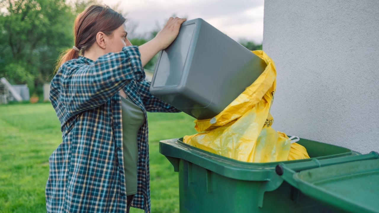 Beautiful young European 30s woman throwing garbage into the trash can in the backyard outdoors near the house