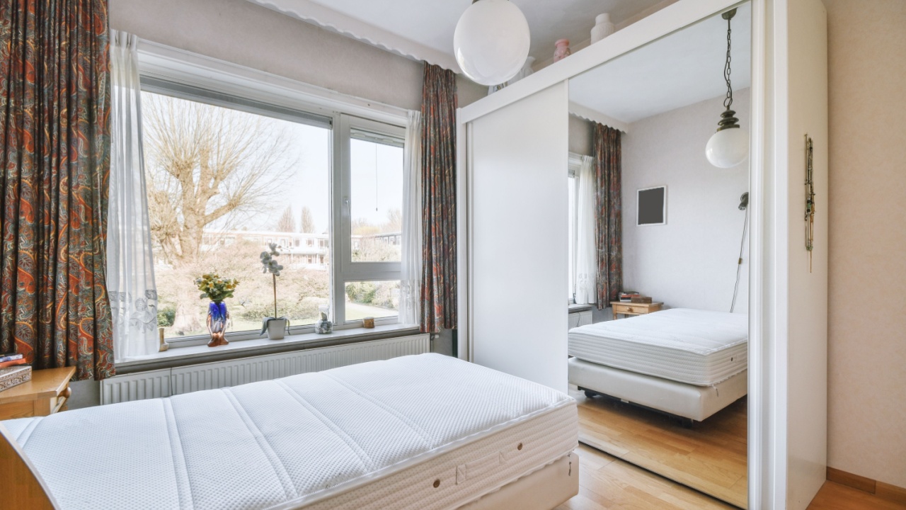 A comfortable bed near a glass bed next to a window and opposite a wardrobe with a mirror in a bright bedroom