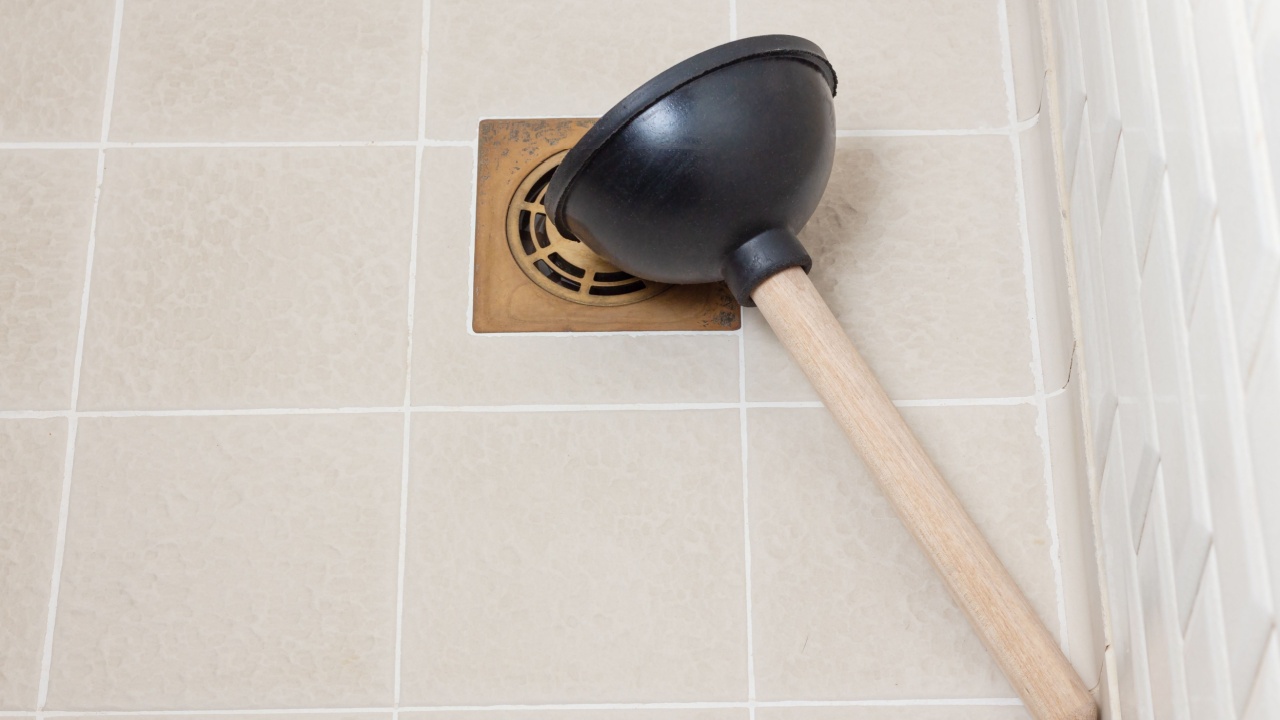 Rubber plunger with wooden handle on the shower floor. Clearing blockages