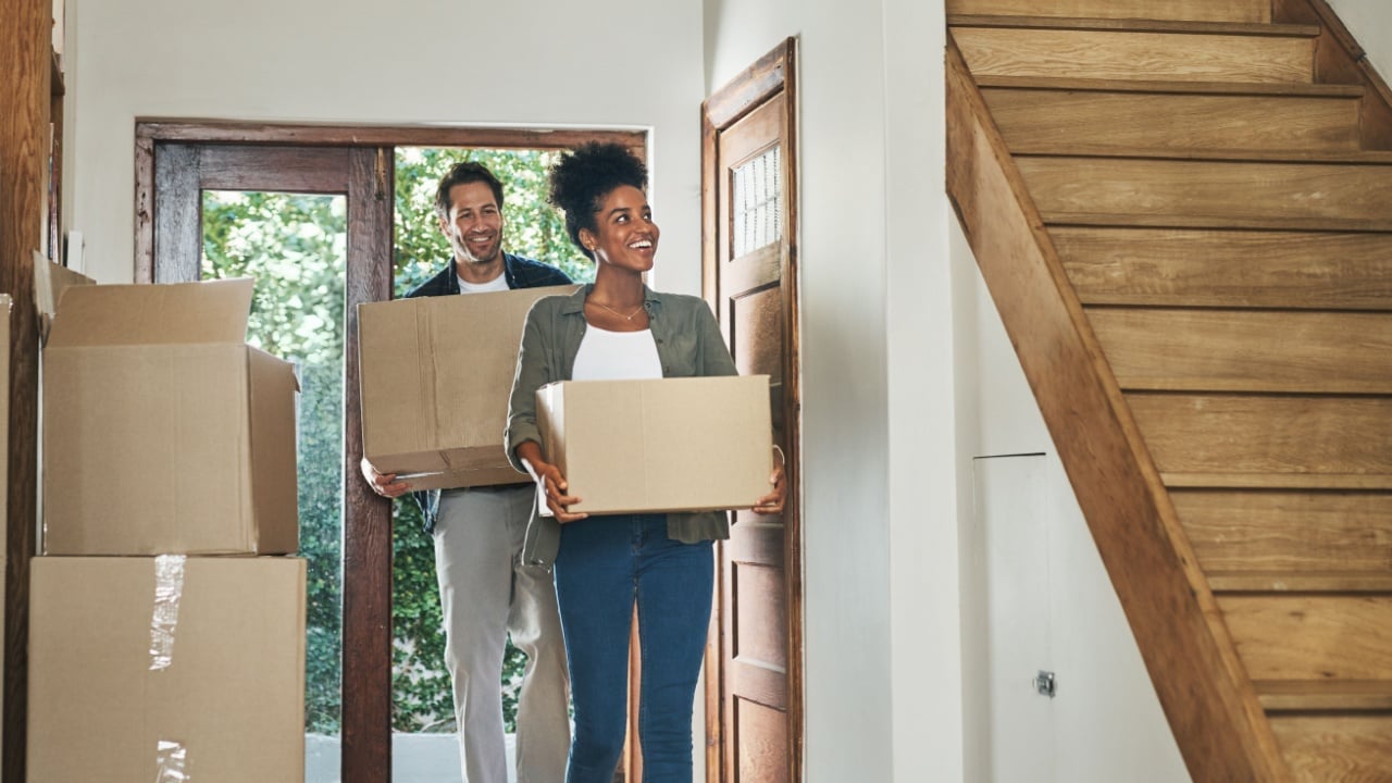 Interracial couple moving into a new modern house, carrying boxes and arriving home together. Happy, excited and smiling husband and wife walking, entering and relocating after buying an apartment