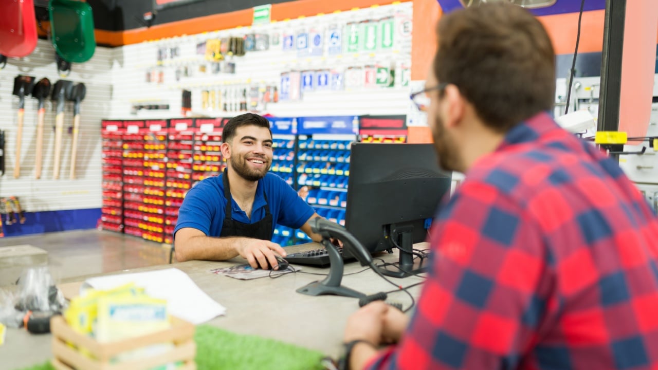 Cheerful young man helping a client at the cashier and talking about new tool products at the hardware store