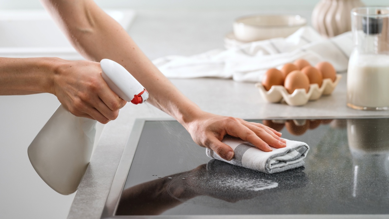 cropped shot of female hands wash electric hob with spray bottle and fabric rag at modern kitchen, care of domestic appliance and housework concept