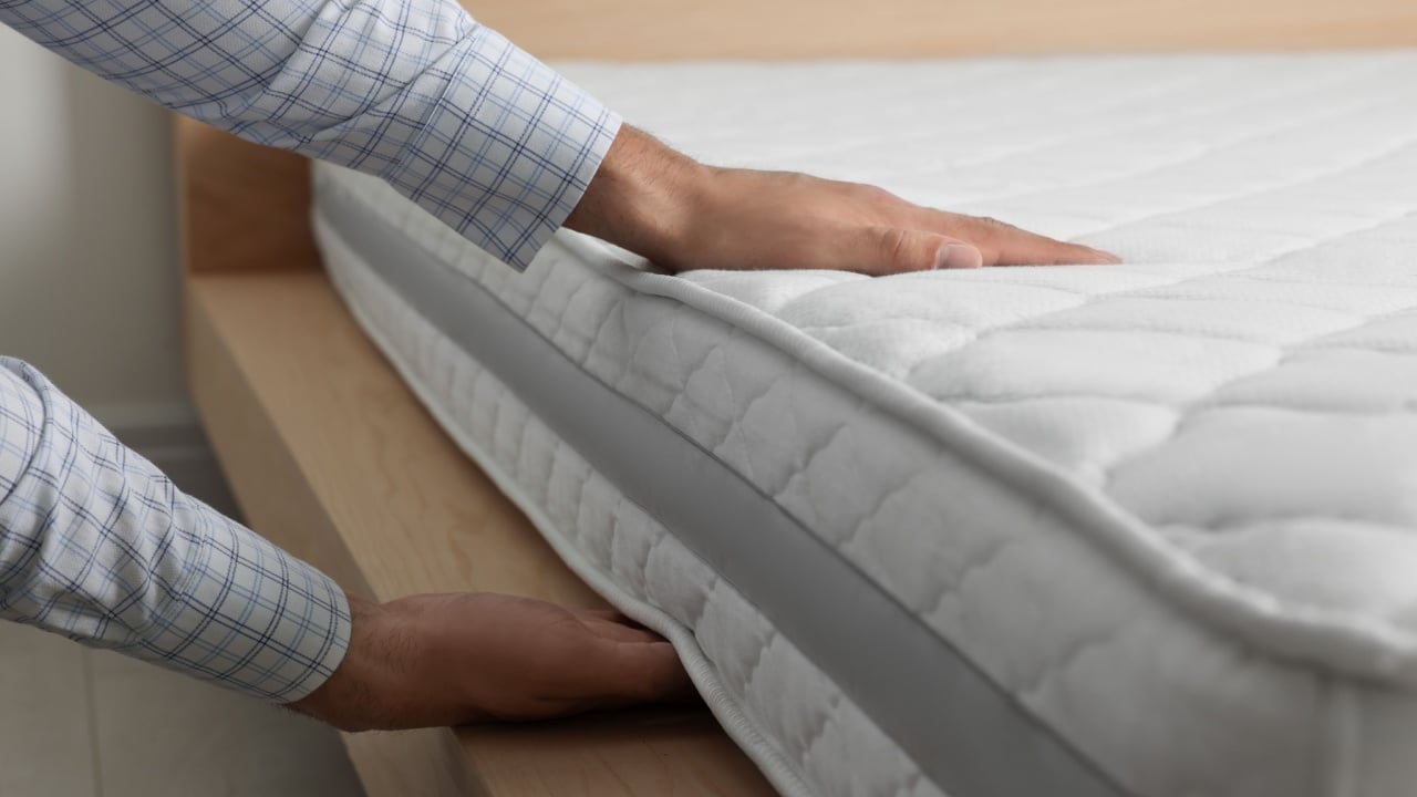 Man touching soft white mattress indoors, closeup