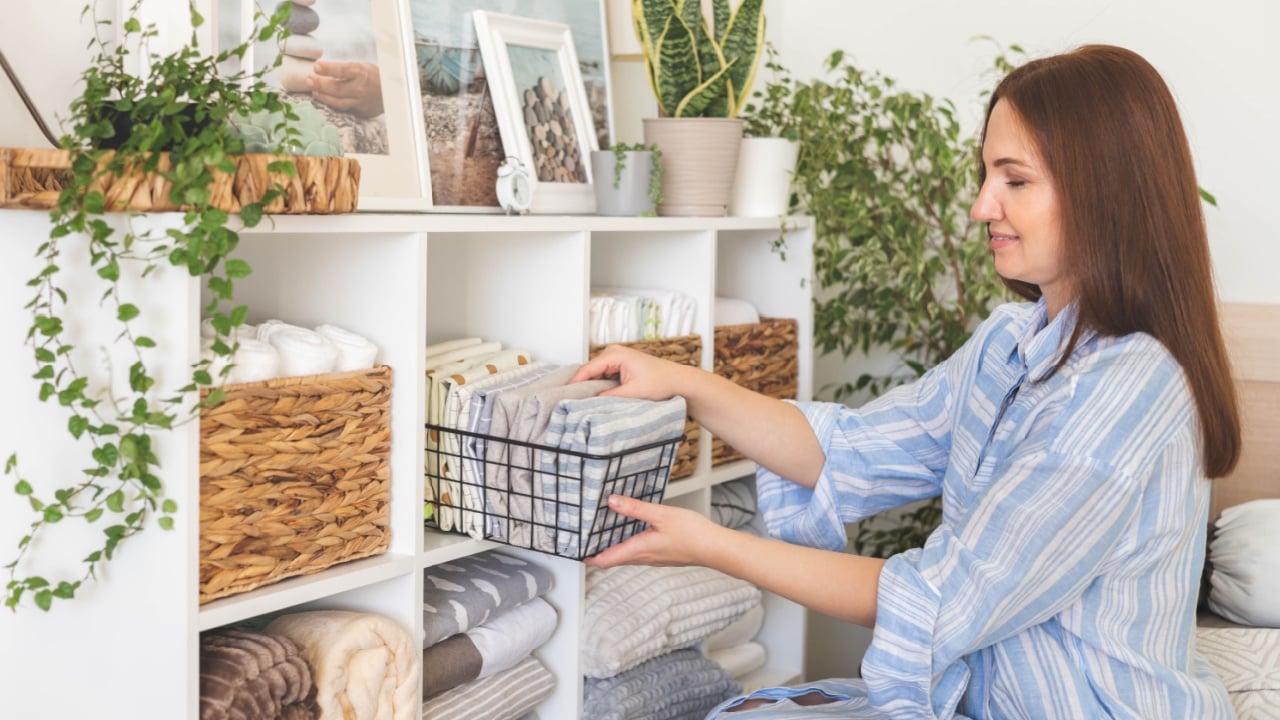 Modern housewife putting neatly folded towels, pillowcases, duvet covers into plastic metallic case boxes use vertical method storage organization. Woman making seasonal tidying up at home cupboard