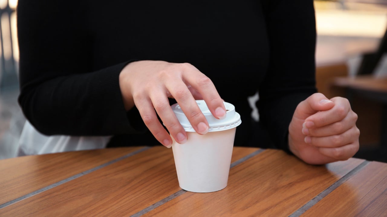 Woman with cardboard cup of coffee at table outdoors, closeup