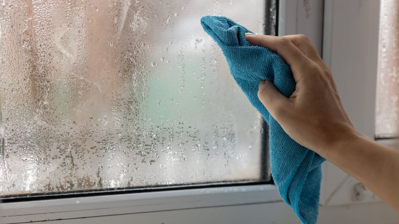 A womans hand wipes the condensate from the window glass with a towel.