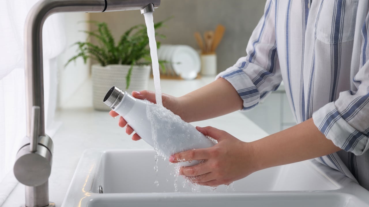 Woman washing thermo bottle in kitchen, closeup