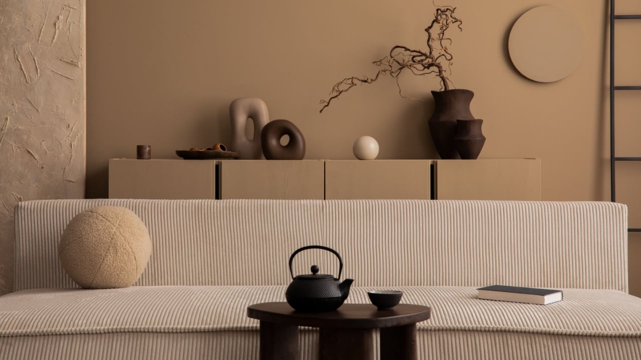 Minimalist composition of warm living room interior with modular sofa, wooden coffee table, round pillows, vase with branch, ladder, books, sculpture and personal accessories. Home decor. Template.