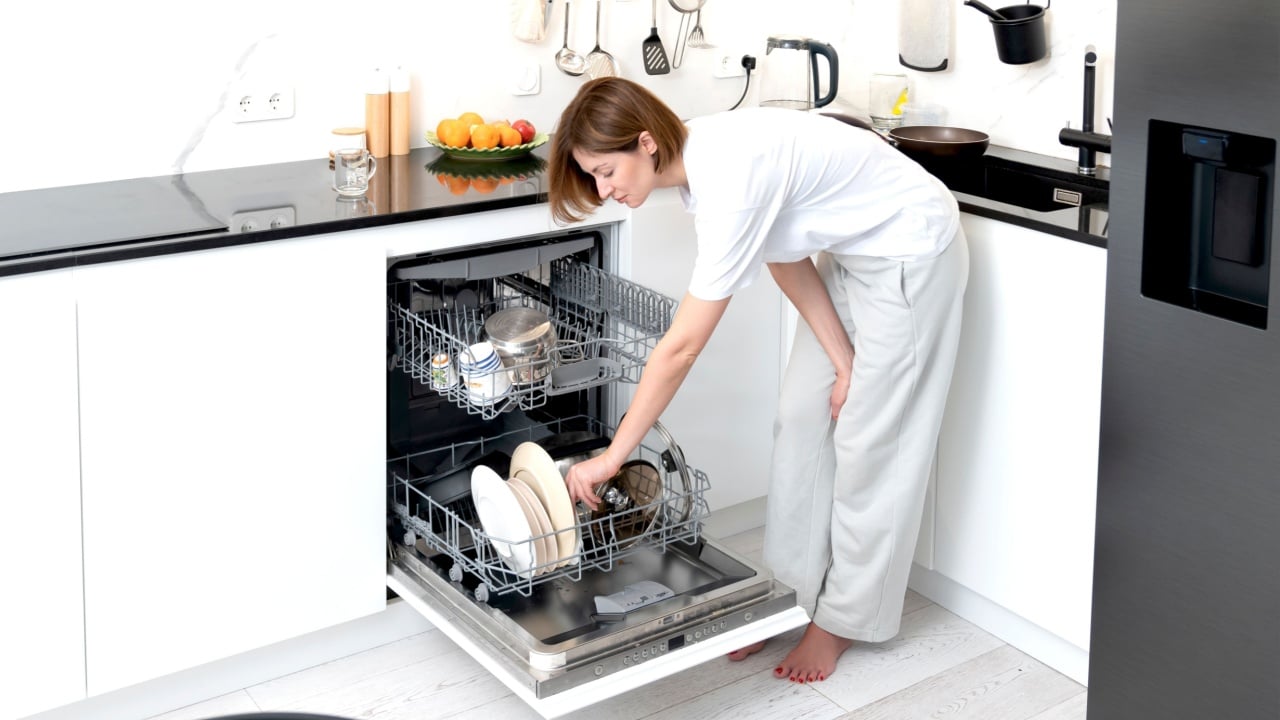 Busy housewife putting dirty plates in dishwasher machine in the kitchen. Household and exhausting cleaning day concept