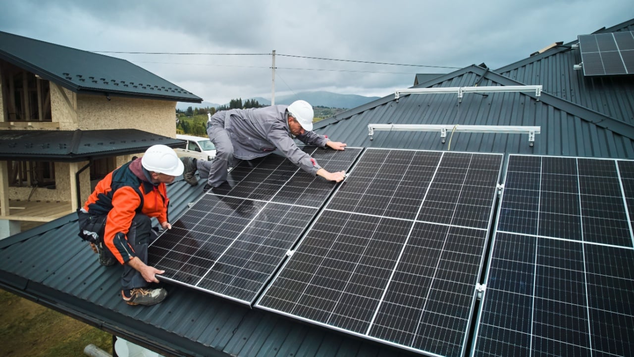 Workers installing photovoltaic solar panels on roof of house. Men engineers in helmets building solar module system with help of hex key. Concept of alternative, renewable energy.