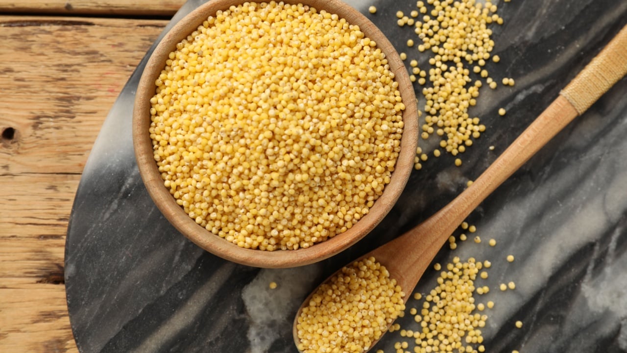 Millet groats in bowl and spoon on wooden table, flat lay