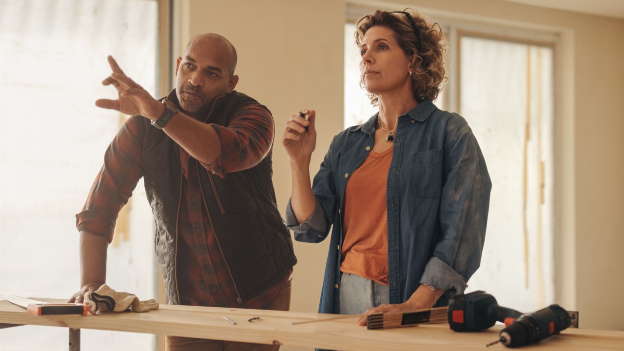 Homeowning couple collaborating on a home renovation project, discussing ideas and planning together. They work diligently indoors, engaging in carpentry and remodeling using wooden planks.