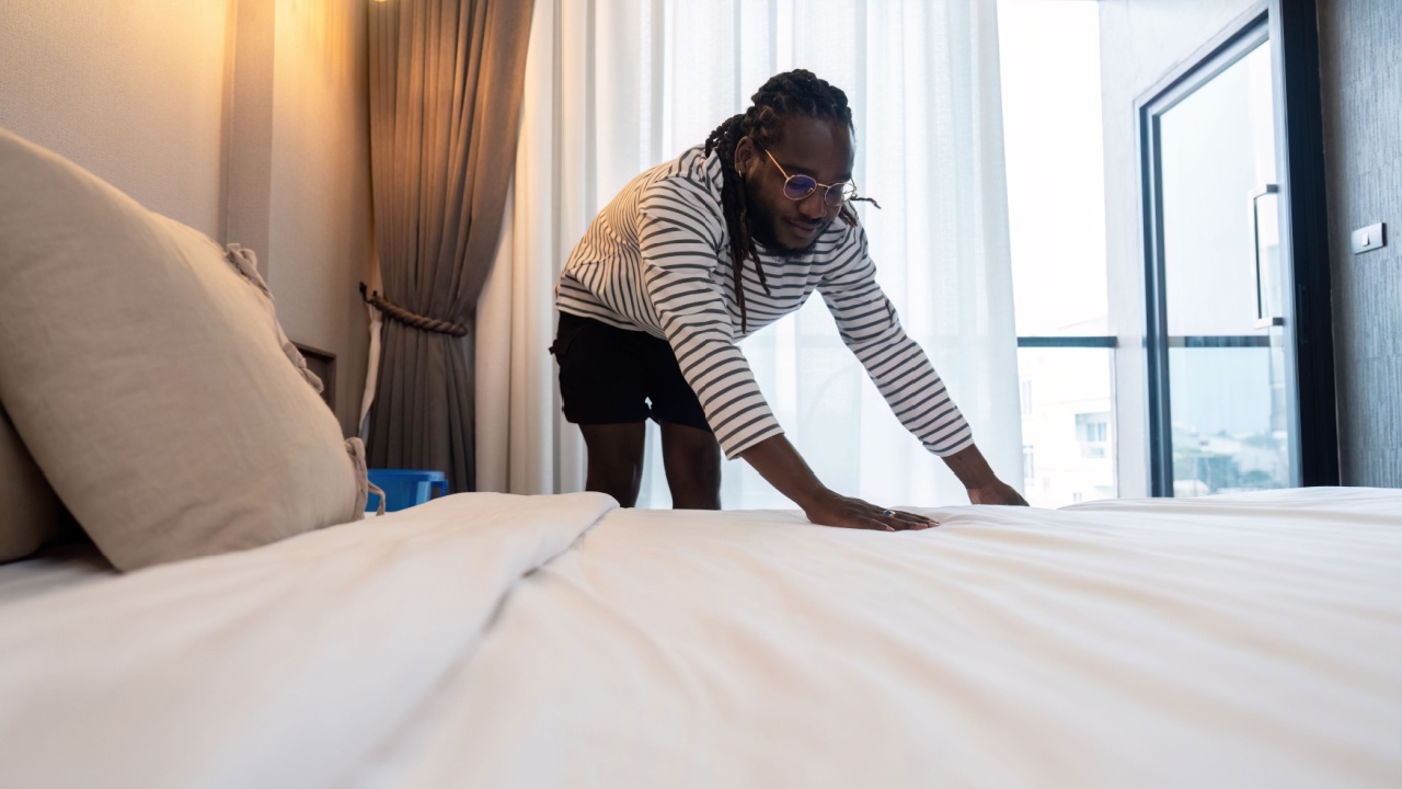 Young African American man clean making bed. happy black man changing bedsheets at home standing in bedroom