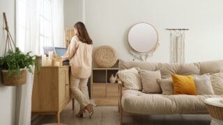 Young woman with record player on commode in cozy living room, back view