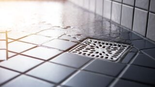 Water flowing to square shower drain hygiene and clean on tiled floor of modern enclosure in bathroom.