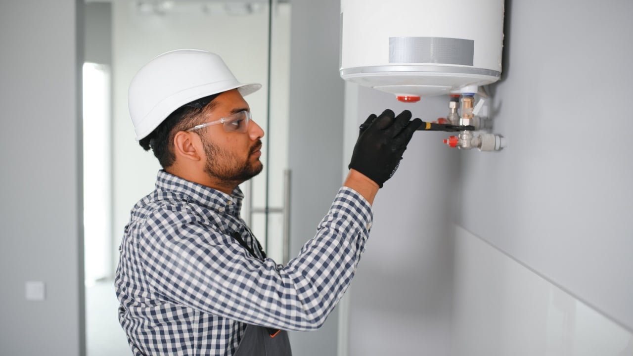 indian plumber using screwdriver while fixing boiler or water heater, working on heating system in apartment.