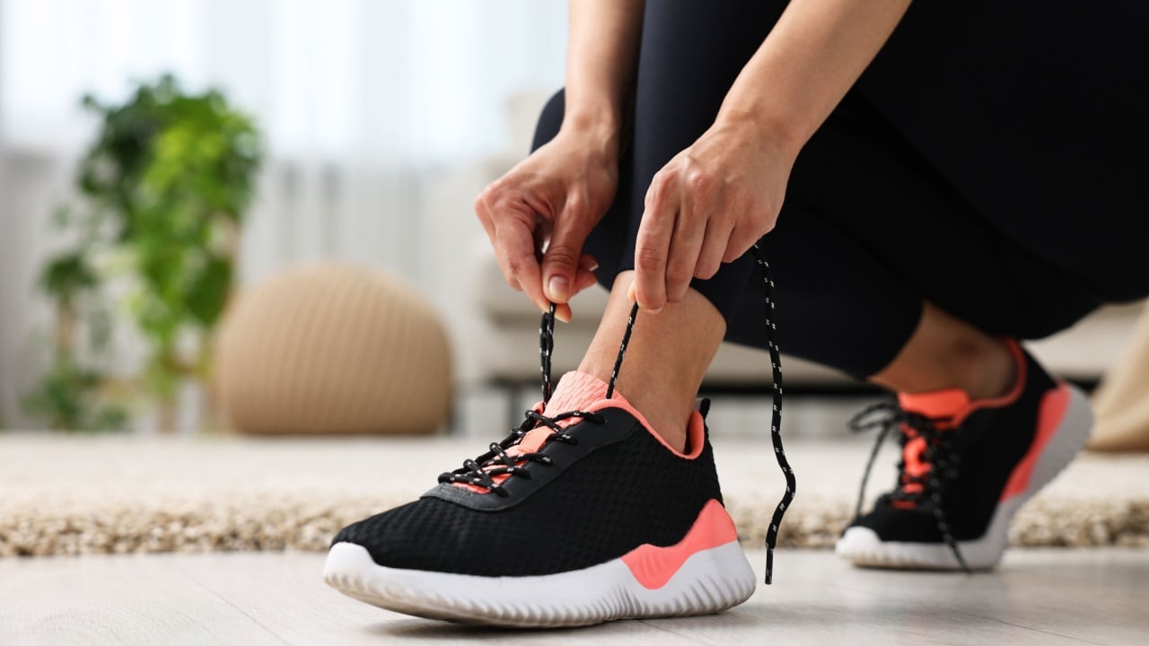 Woman tying shoelace of sneaker indoors, closeup.