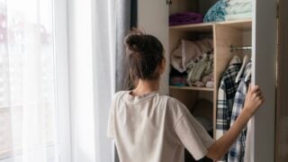 A woman stands in front of her wardrobe closet, carefully choosing clothes in a well-lit space during the day
