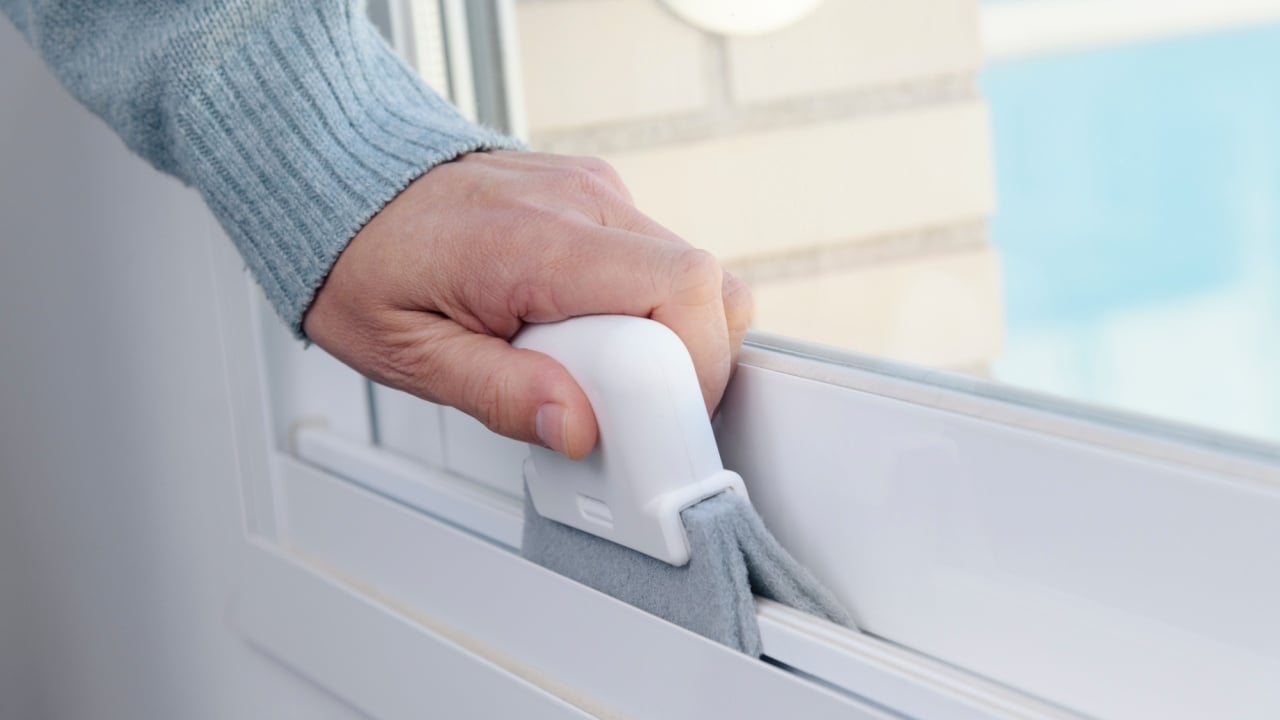 closeup of a man cleaning the track of a white sliding window frame using a cleaning device