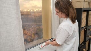 Woman sealing window frame with caulking gun indoors.
