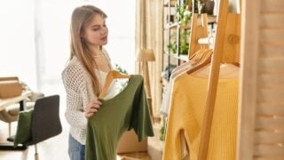 A young woman sorts through her clothes, preparing items for donation in a bright space.