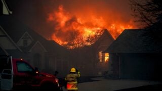 A firefighter stands near burning residences during a wildfire outbreak in Stillwater, Oklahoma, as efforts to control the destructive flames continue.