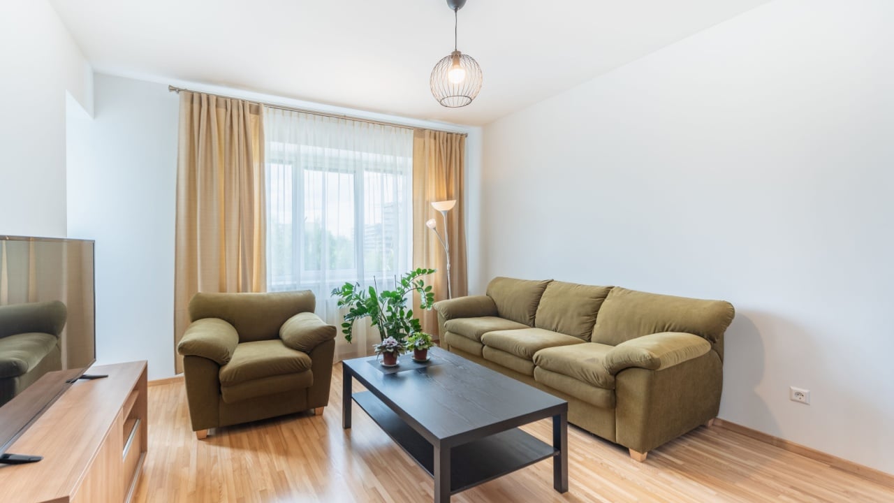 A sophisticated yet cozy living room featuring olive-colored couches, a black table, a wooden entertainment unit, and natural light through wide windows