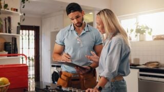 Woman, man and plumber with clipboard in kitchen for invoice, report and talk for repair at house. People, handyman and client with checklist for drainage system, inspection and leak at apartment