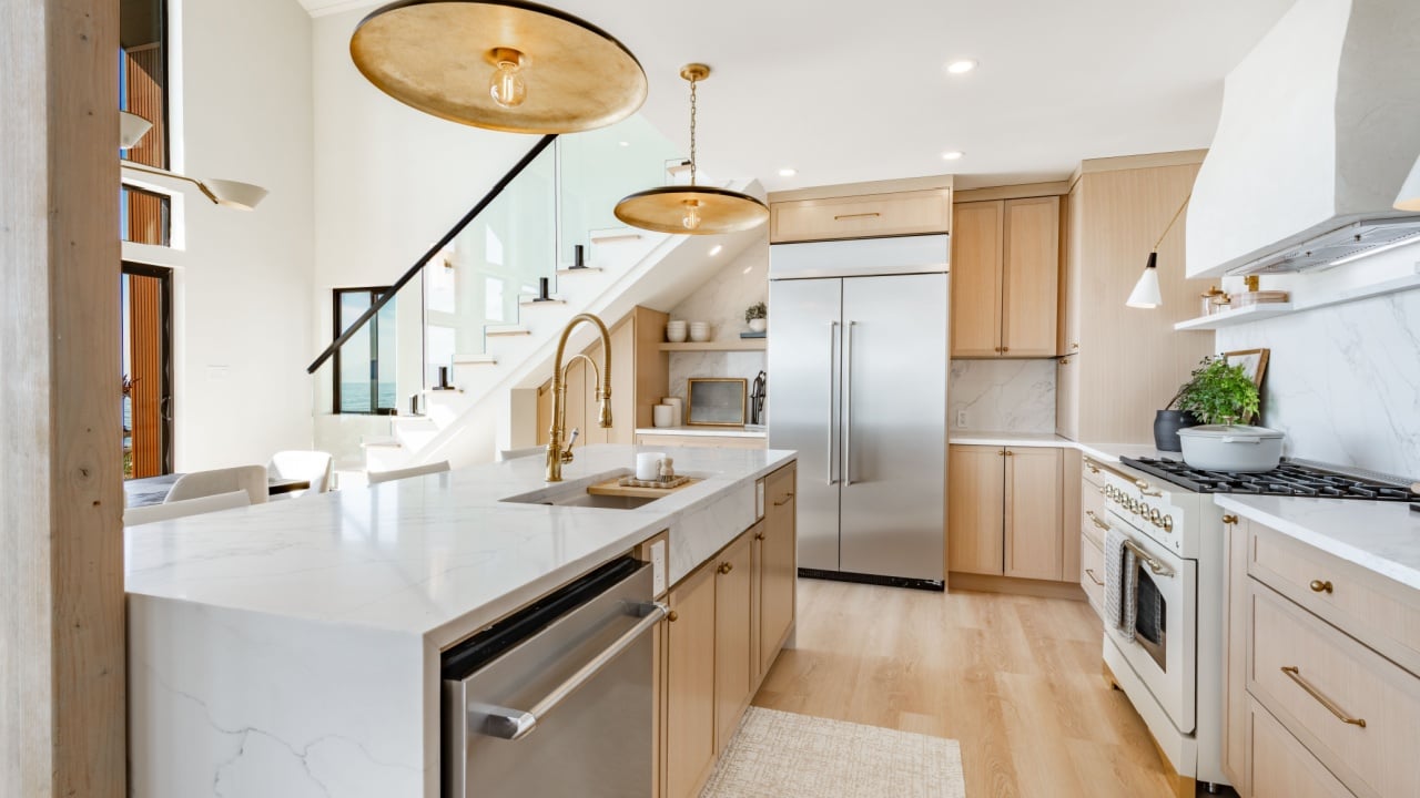 Large kitchen dining room interior white marble countertops brass light fixtures modern oven and stainless steel appliance ocean view floor to ceiling windows hardwood floor modern spacious design