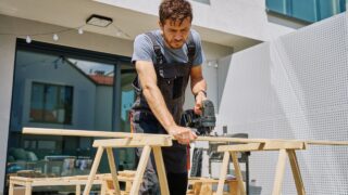 Man cutting wooden plank with electric jigsaw at home backyard. Outdoor carpentry and DIY work
